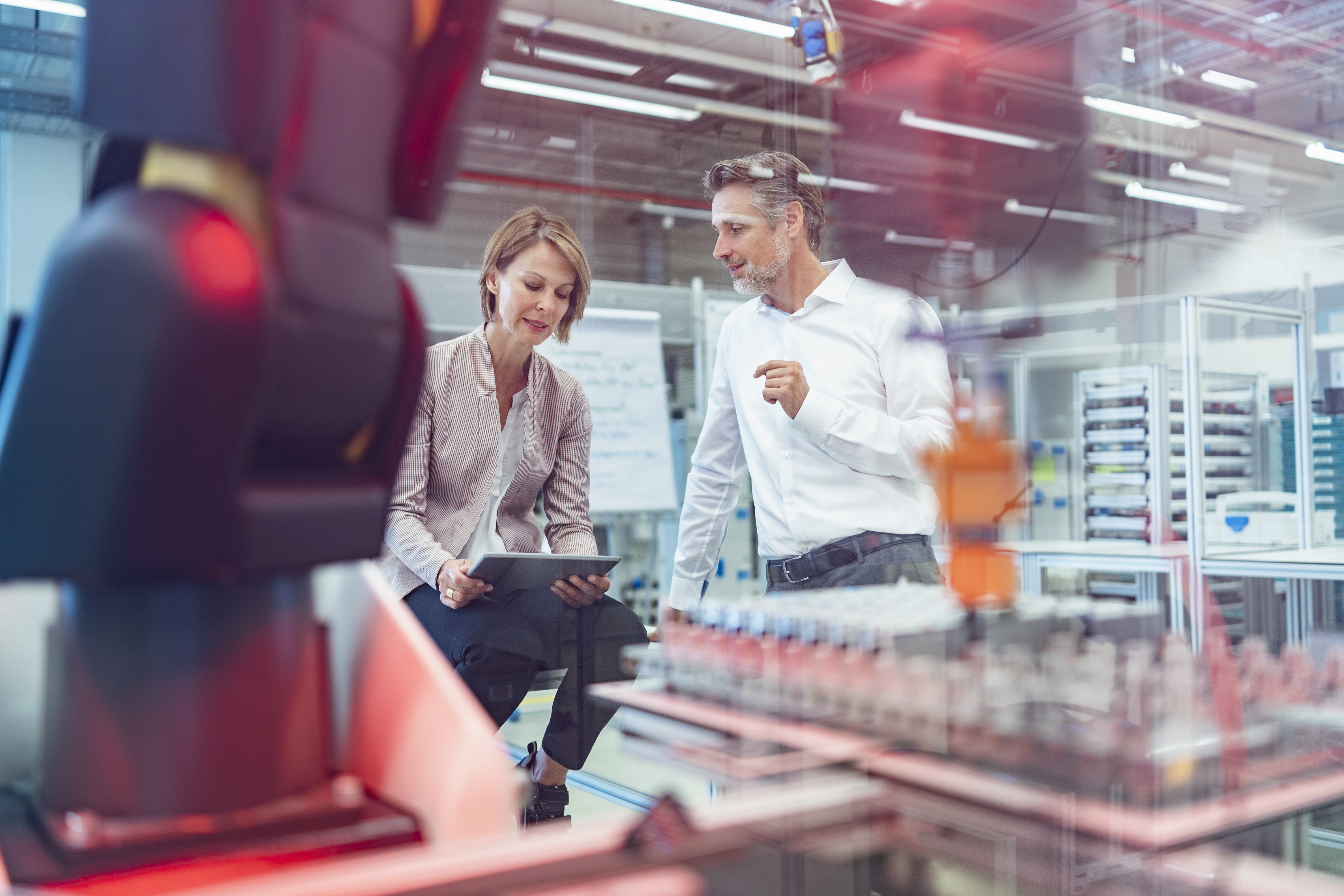 Zwei Personen diskutieren in moderner Fabrik neben einem Industrieroboter.