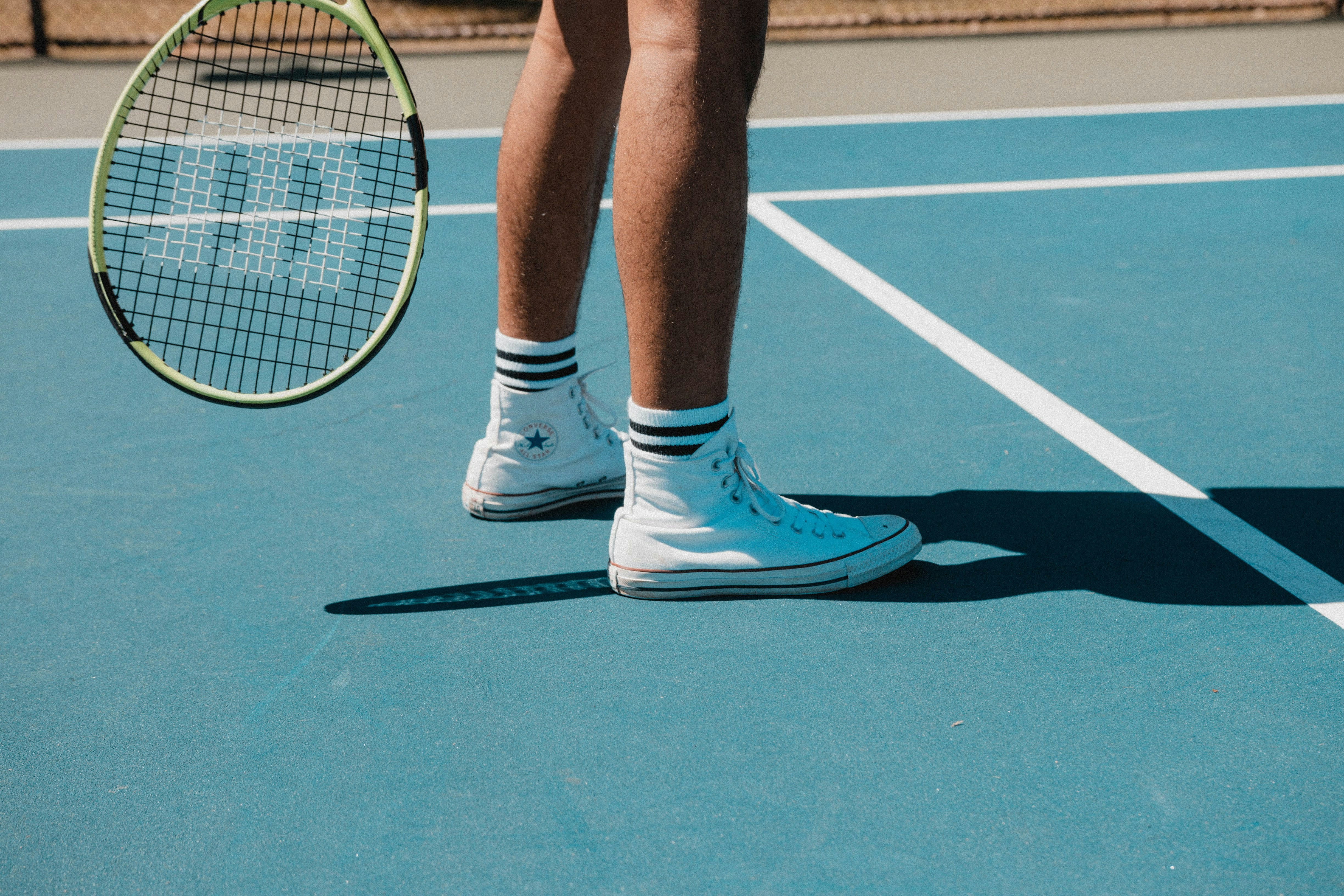 Tennisspielerbeine mit Schl&auml;ger auf blauem Platz, wei&szlig;e Turnschuhe und Socken